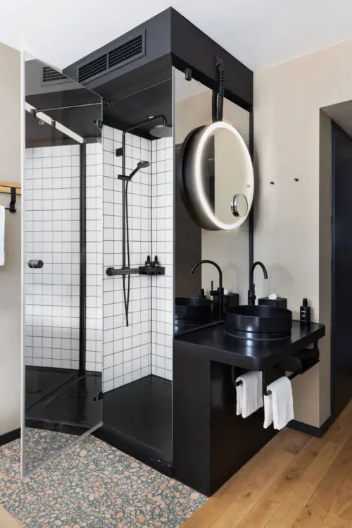 Offene Dusche mit rundem Spiegel über schwarzem Waschbecken und Handtüchern in modernem Bad.