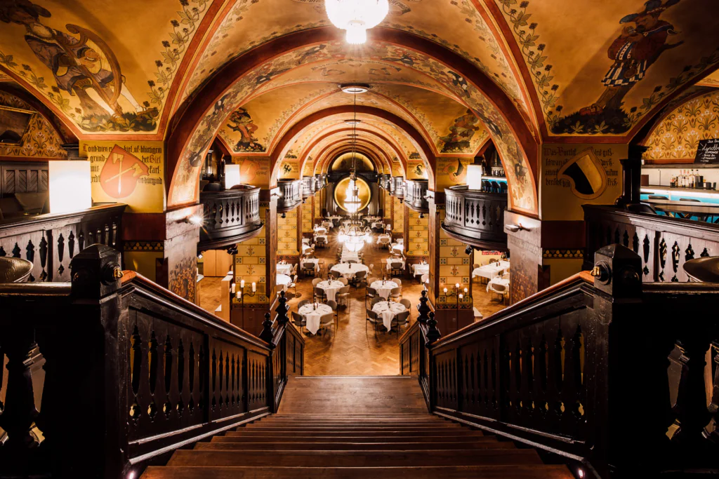 Salle de restaurant somptueuse avec voûtes, fresques murales et tables dressées – ambiance élégante et historique.