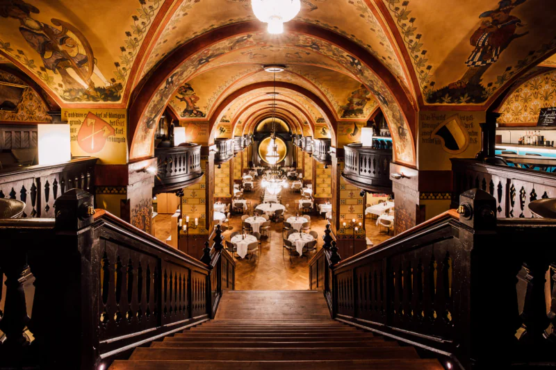 Grand restaurant hall with vaulted ceiling, murals and set tables – elegant, historic atmosphere.