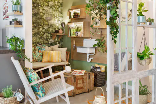 Grüne Sitzecke mit Holzbank, Sessel, kleinem Tisch, Pflanzenwand und Waschbeckenbereich mit Hängepflanzen.