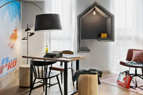 Tisch mit Holzplatte und modernem Lampenschirm, daneben Meetingecke in Hausform mit integrierter Beleuchtung.