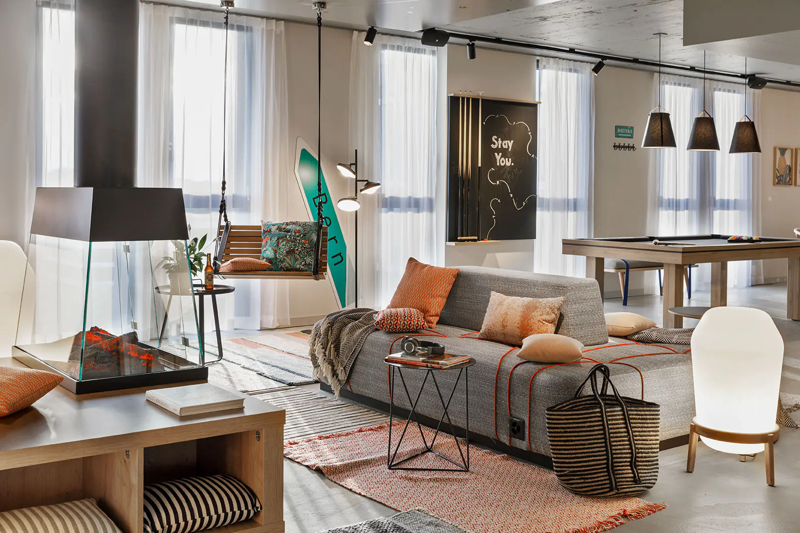 Cozy lounge with fireplace, large grey sofa, hanging chair and pool table in the background.