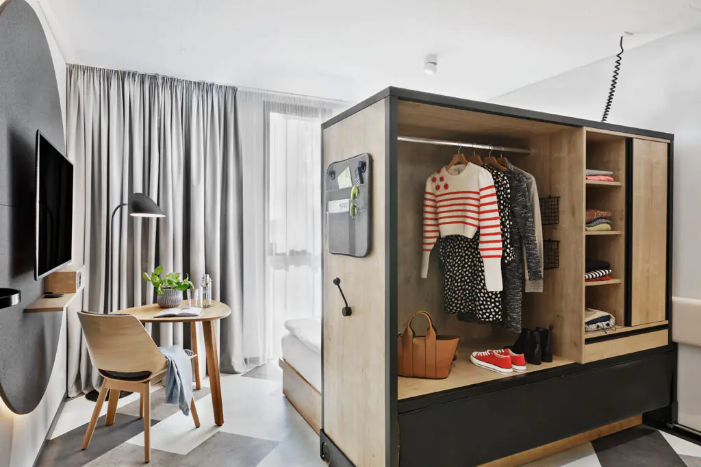 Studio mit multifunktionalem Möbel: offenes Verschiebeelement mit Garderobe, Sitzbereich und Fensterfront.