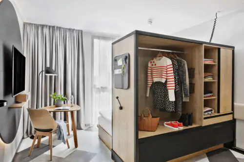 Studio mit multifunktionalem Möbel: offenes Verschiebeelement mit Garderobe, Sitzbereich und Fensterfront.