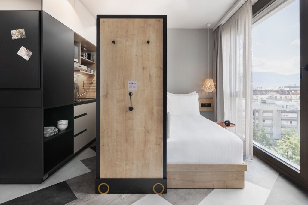 Studio mit Bett, trennendem Verschiebeelement, Küchenzeile und großem Fenster mit Blick auf die Stadt.