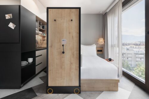 Studio mit Bett, trennendem Verschiebeelement, Küchenzeile und großem Fenster mit Blick auf die Stadt.