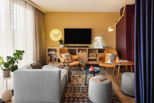 Gaming area im Aufenthaltsbereich mit Sofas, Fernseher, Teppich und Regal mit Brettspielen.