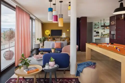 Compact kitchenette in light wood with cooktop, microwave and sink, with entrance area in the background.