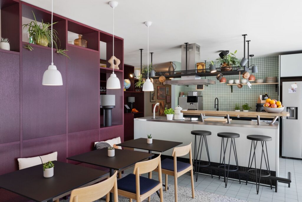 Gemeinschaftsküche mit offenen Regalen, Hängelampen und hellen Holzmöbeln im modernen Raumdesign.