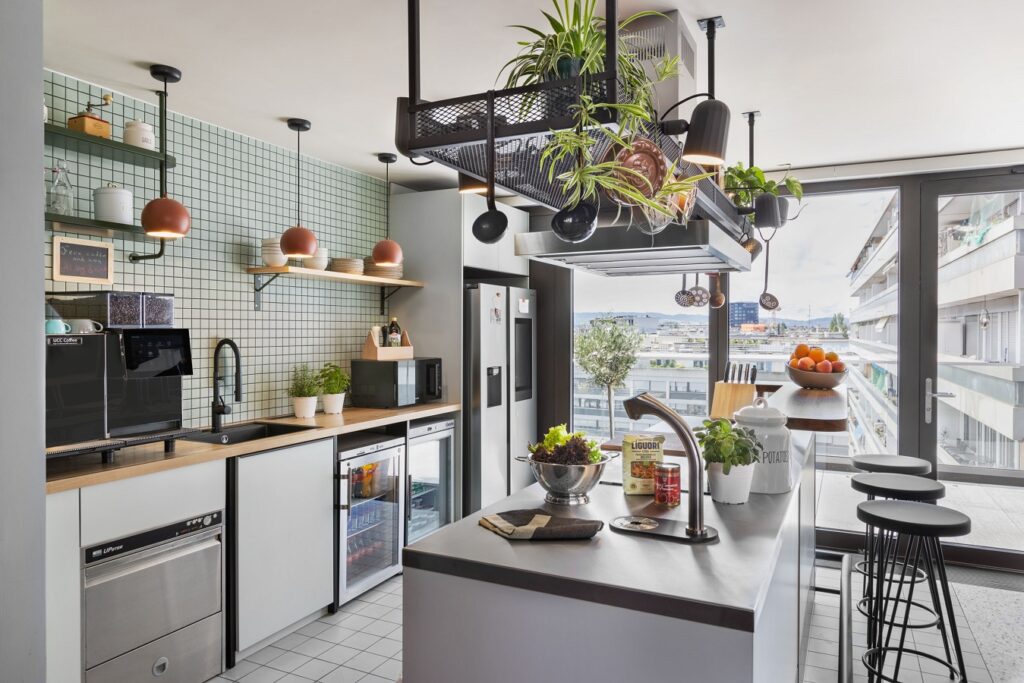 Zentrale Kücheninsel mit Wasserspender, Kaffeemaschine, Kühlschrank, Kochfeld und frischem Obst.