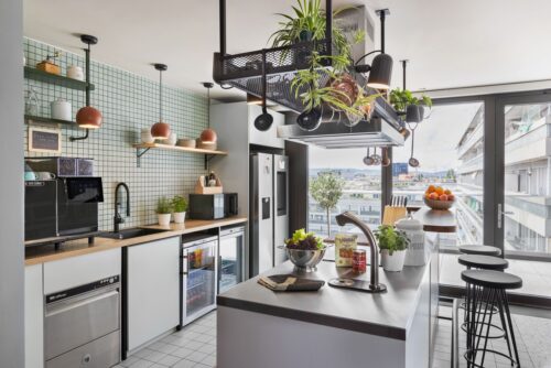 Zentrale Kücheninsel mit Wasserspender, Kaffeemaschine, Kühlschrank, Kochfeld und frischem Obst.