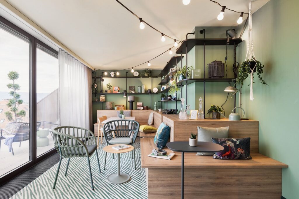 Inviting loggia with green wall, sofa, cushions and shelves with plants and decorative elements.