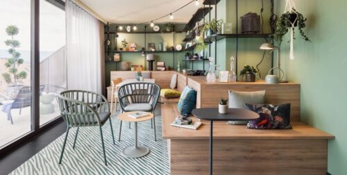 Einladende Loggia mit grüner Wand, Sofa, Kissen und Regalen mit Pflanzen und dekorativen Elementen.