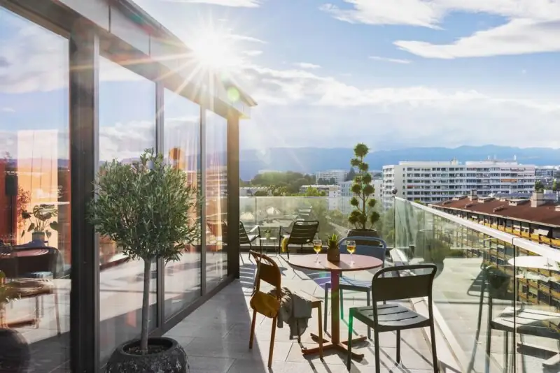Sunny rooftop terrace with modern glass front, seating areas and wide city views in a relaxed setting.