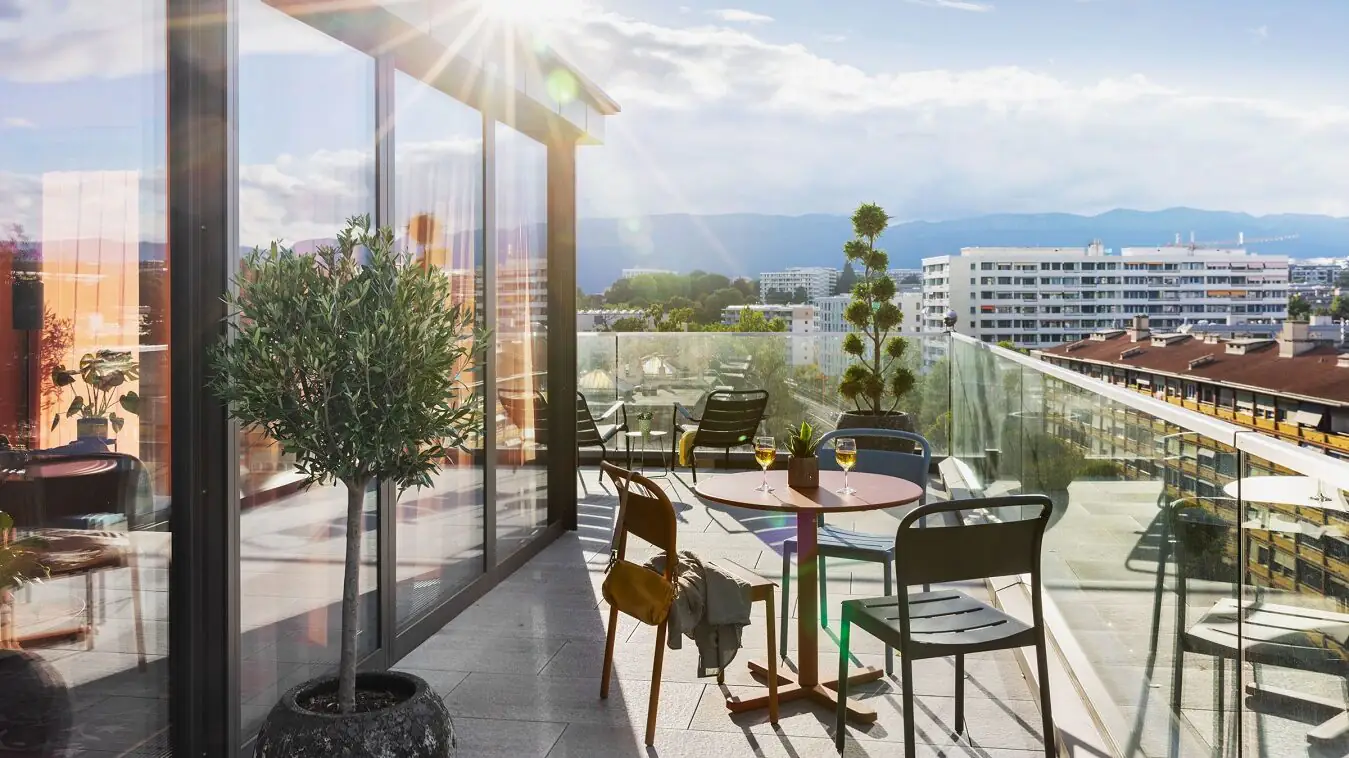 Sunny rooftop terrace with modern glass front, seating areas and wide city views in a relaxed setting.
