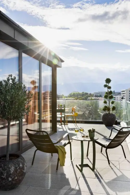 Sunny rooftop terrace with modern glass front, seating areas and wide city views in a relaxed setting.