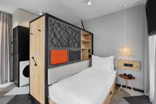 Sleeping area with bed, sliding unit and bedside table with hanging lamp, washing machine visible behind.