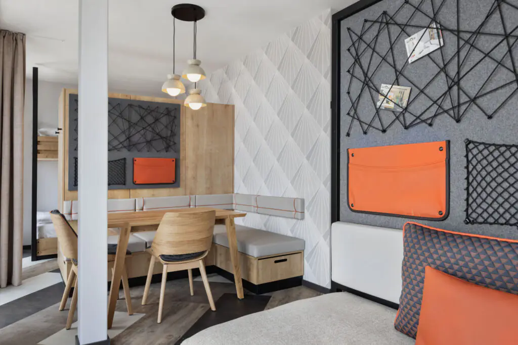Dining or workspace with wooden table, chairs, bench and wall with geometric wallpaper.
