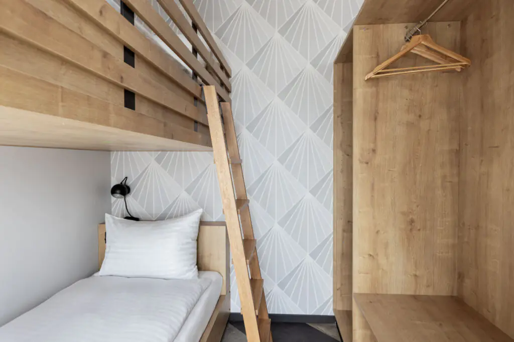 Bunk bed with light wooden frame and open wardrobe as a practical sleeping solution in the studio.