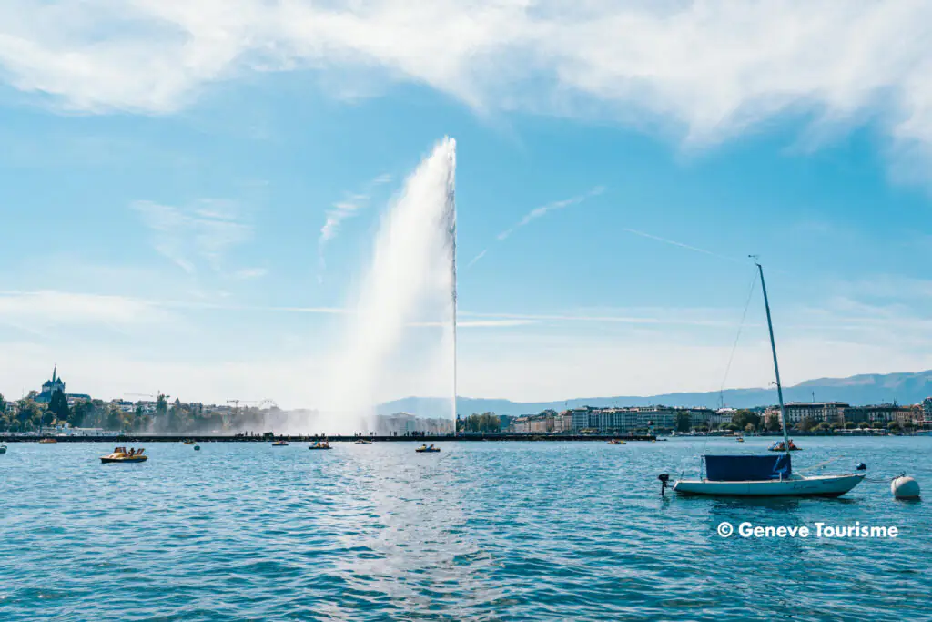 Jet d’Eau am Genfersee in Genf mit Segelboot und Blick auf die Uferpromenade.