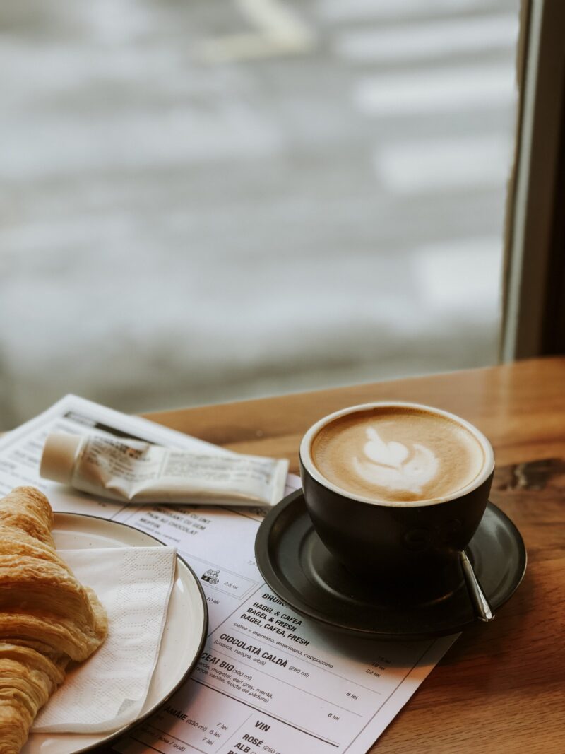Cappuccino mit Latte Art und Croissant auf einem Tisch in einem Café.