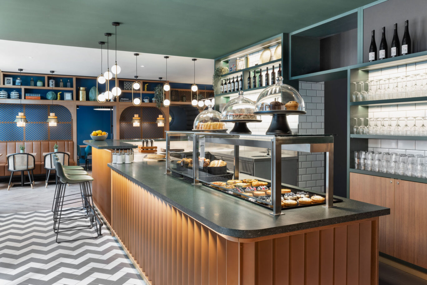 Cafébereich mit Theke, Zickzackboden, Vitrine und Regalen im Hintergrund.