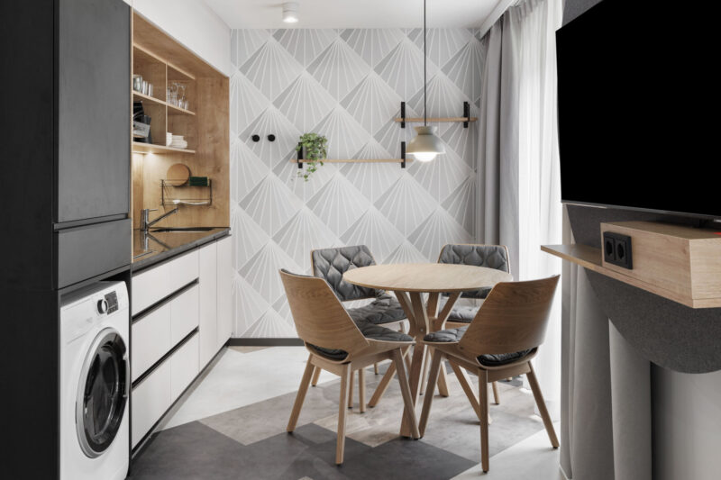 Dining area with a small table and chairs, a hanging lamp above, and a fully equipped kitchen including a washer/dryer and a TV