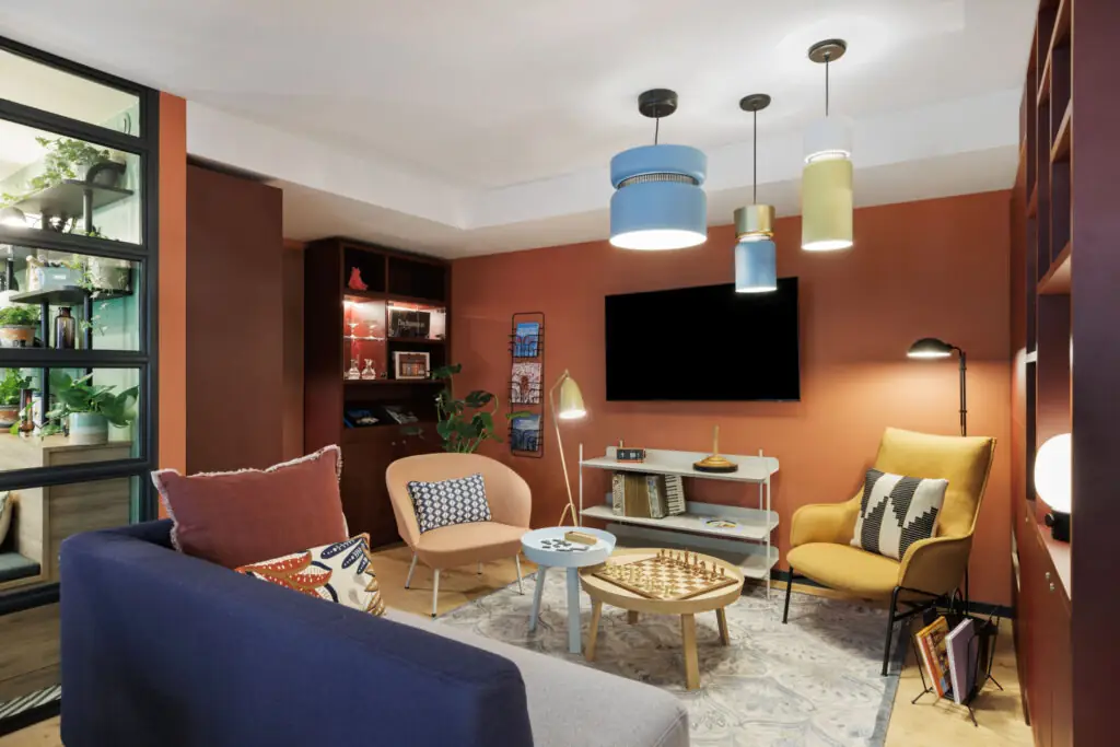 Gemütlicher Gaming Room mit Sitzgelegenheiten, kleinem Tisch mit Schachbrett, Fernseher, Wandregalen mit Brettspielen und Hängelampen