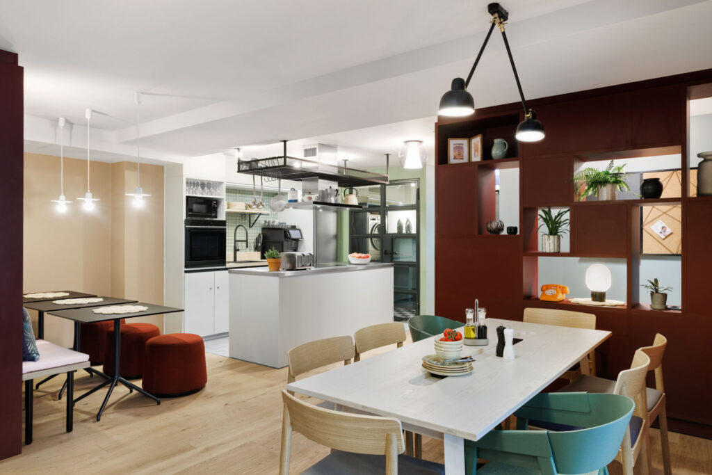 Community table and shelve with decorative elements in the foreground, shared kitchen visible in the background