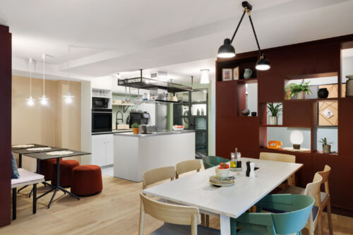 Community table and shelve with decorative elements in the foreground, shared kitchen visible in the background
