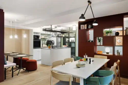 Community table and shelve with decorative elements in the foreground, shared kitchen visible in the background
