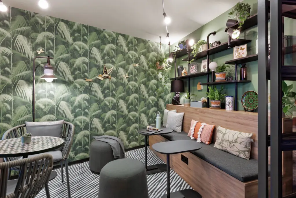 Green loggia with indoor plants, seating, small tables, wall shelf with decorative elements