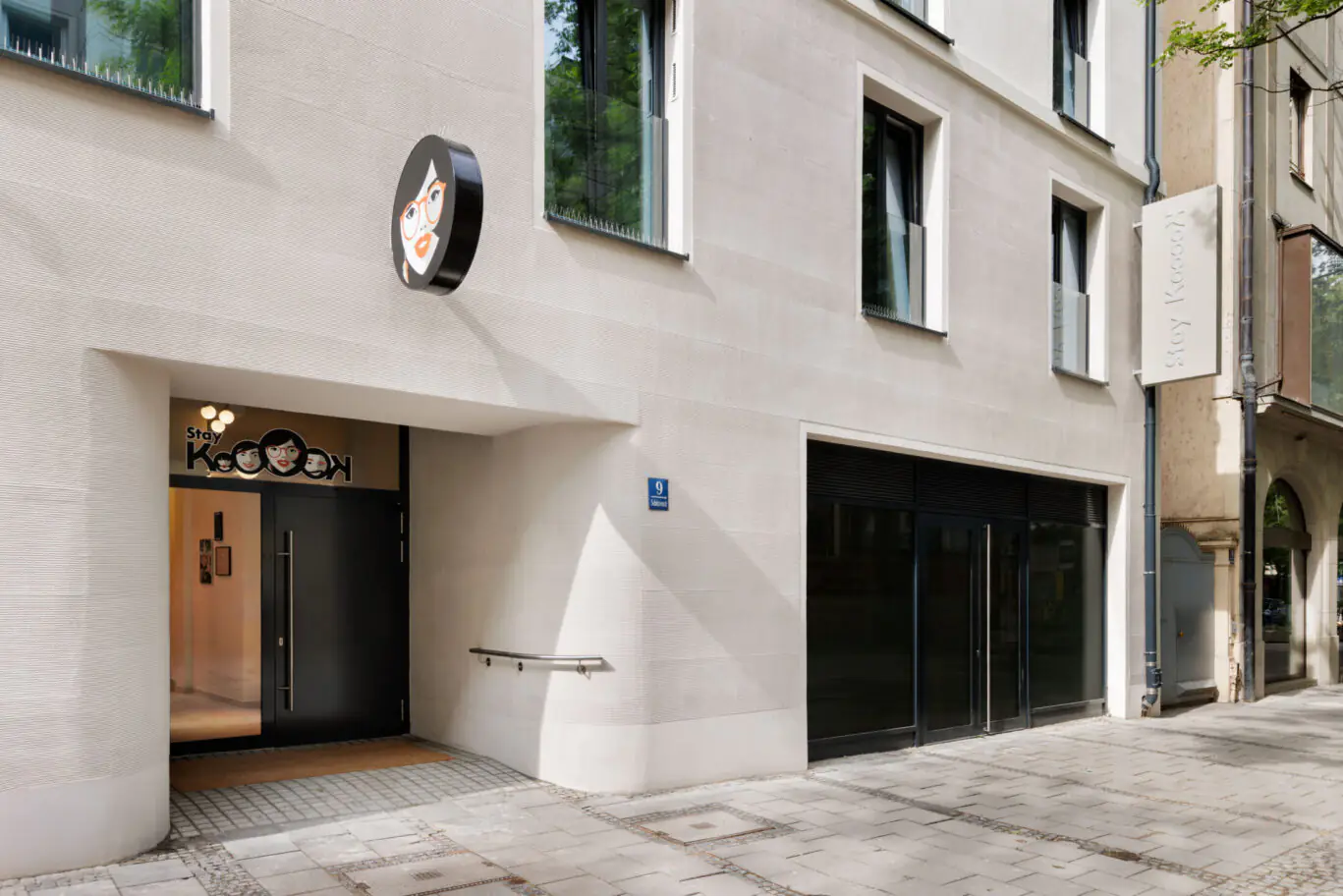 Hotel entrance with illuminated “KoooK” logo above glass door, with ramp and large window front.