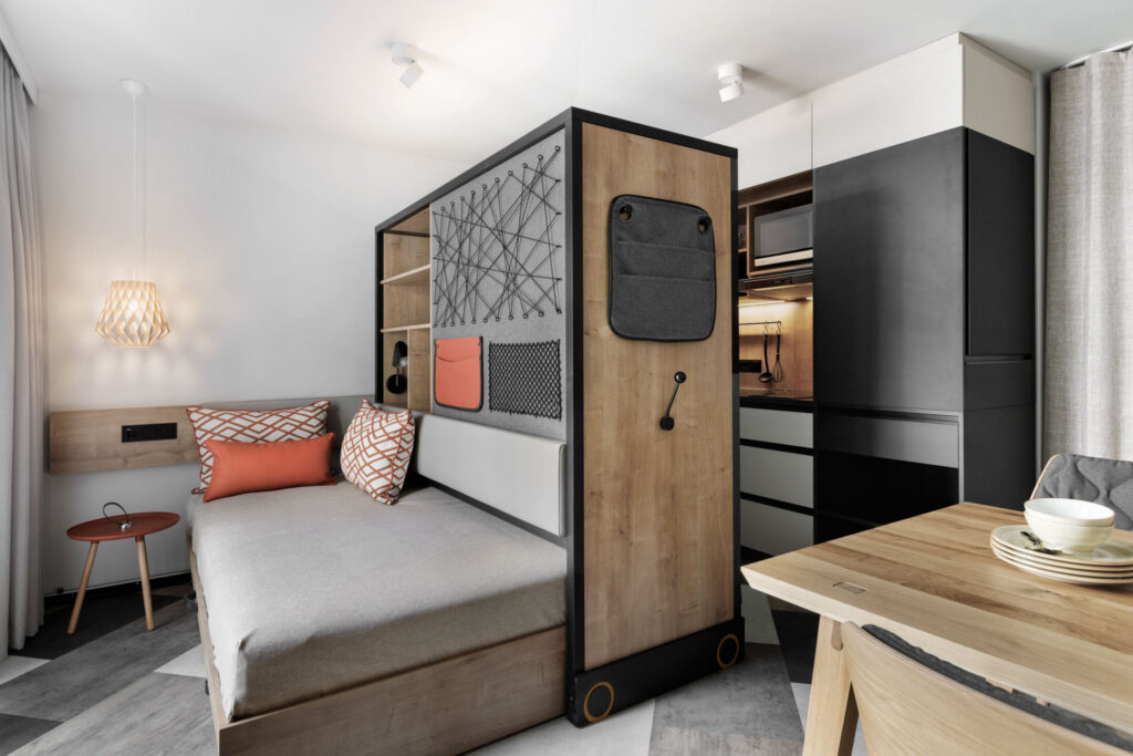 Room divider with bench, bed and wardrobe plus table with tableware in an open living concept.