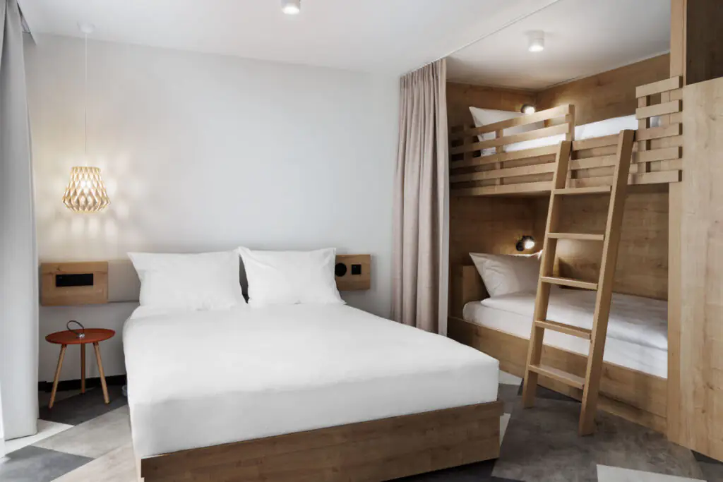 Familienzimmer mit Doppelbett und Etagenbett aus Holz in hellem, minimalistischem Raumdesign.