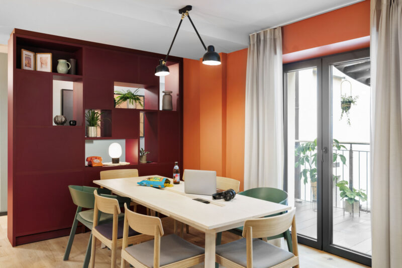Modern dining area with wooden table, laptops and large windows leading to a terrace.