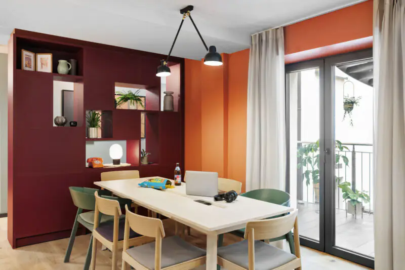 Modern dining area with wooden table, laptops and large windows leading to a terrace.