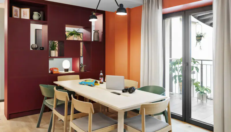 Moderner Essbereich mit Holztisch, Laptops und großen Fenstern mit Zugang zur Terrasse im Hintergrund.