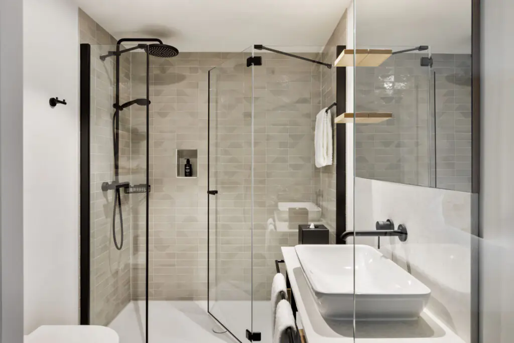 Helles Badezimmer mit begehbarer Dusche, schwarzer Armatur und modernem Waschplatz mit Spiegel.