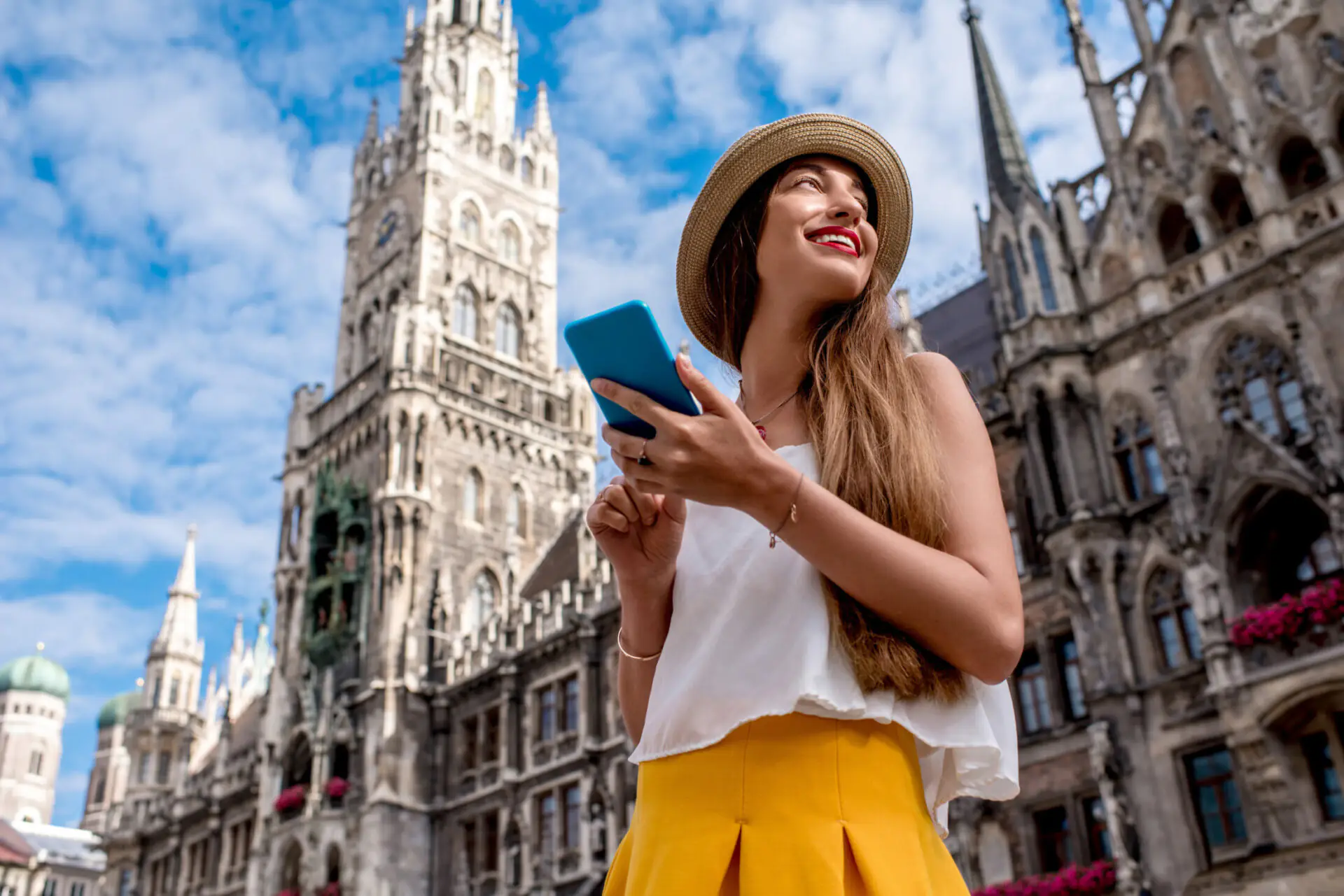 Tourist using smartphone in front of New Town Hall at Marienplatz in Munich on a sunny day.