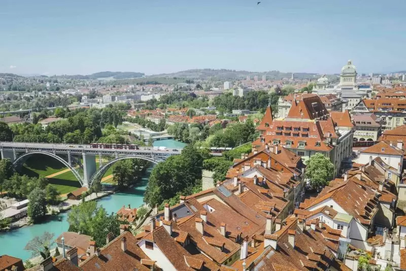 Aerial view of Bern’s old town with red rooftops, the Aare river, and a bridge in the foreground.