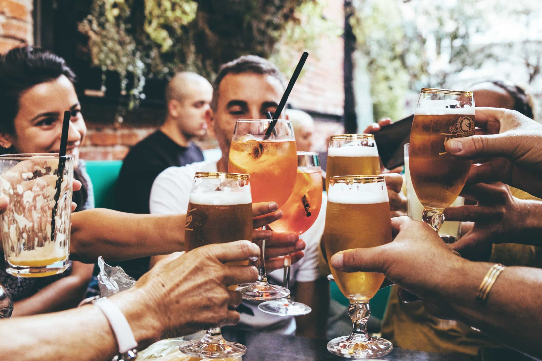 Friends clink beers and aperol outdoors, enjoying relaxed moments together in a social atmosphere.