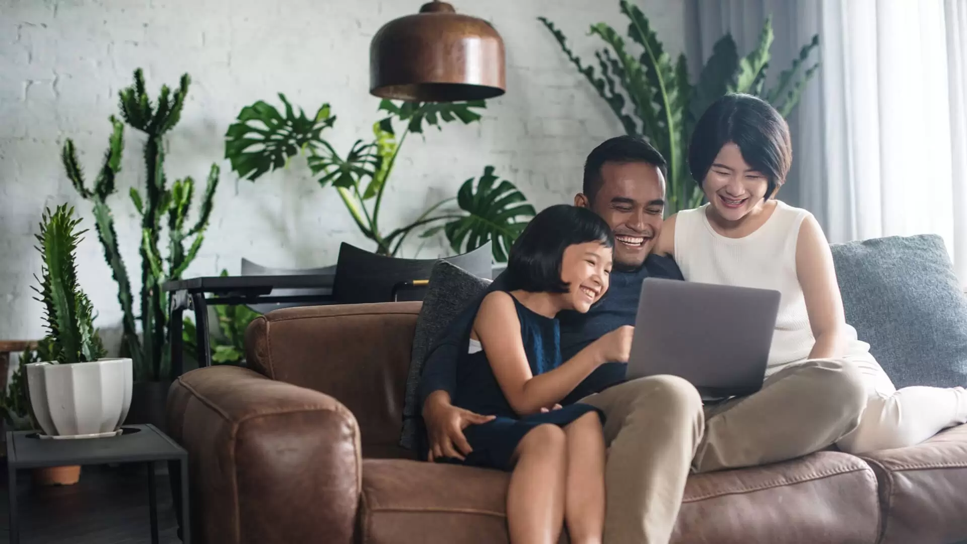 A family consisting of a father, mother and child are looking at a laptop and laughing