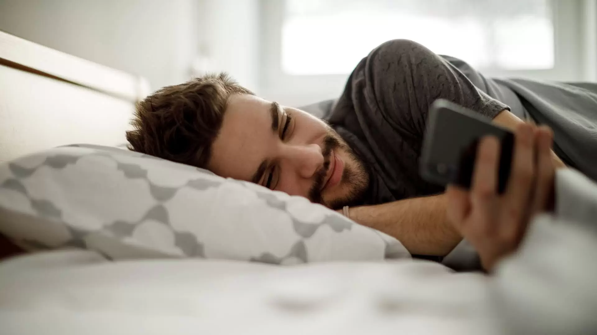 A man is lying in bed and is on his mobile phone
