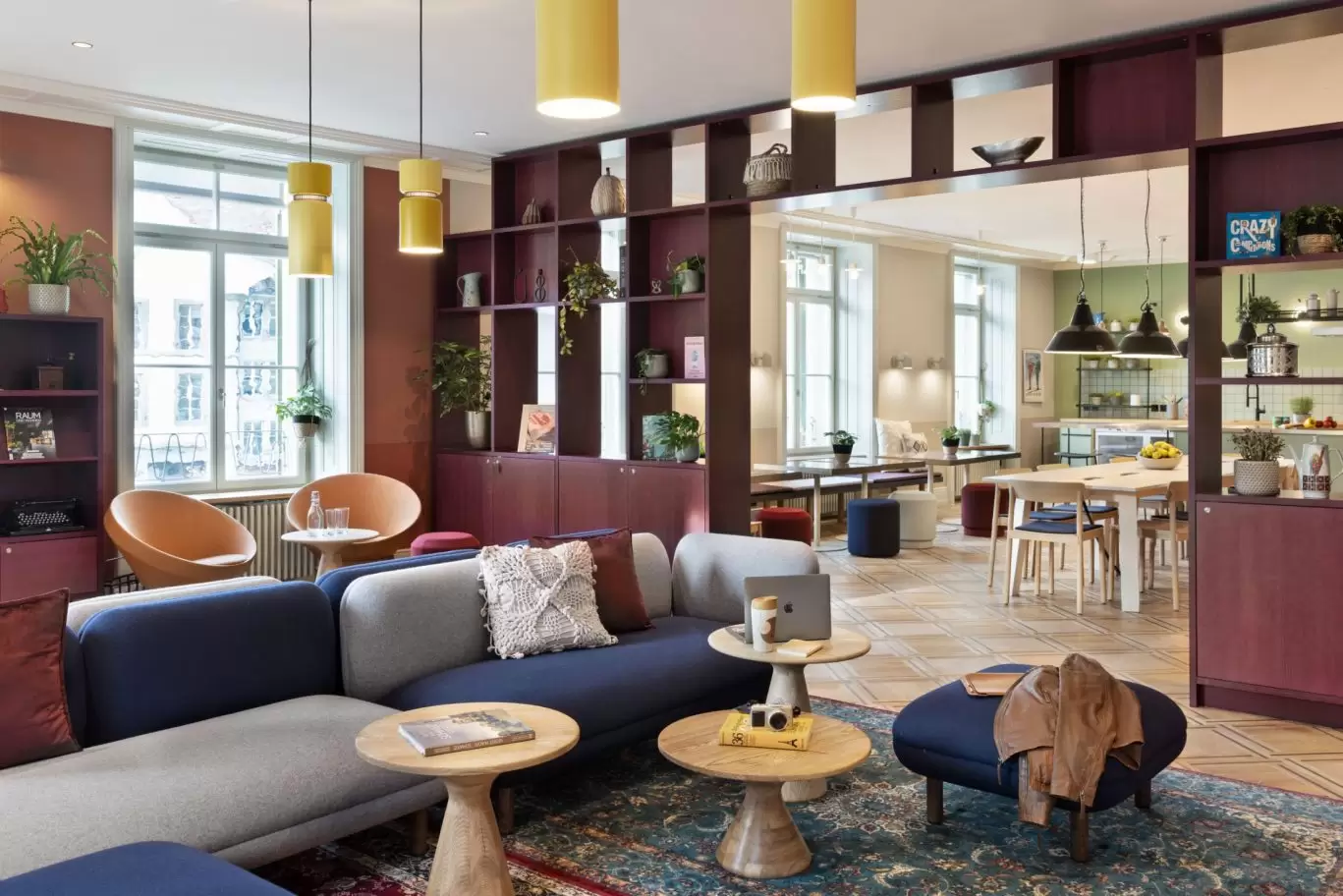 Lounge mit modularen Sofas in Blau und Terracotta, Holztischen und Wandregal in warmer Atmosphäre.
