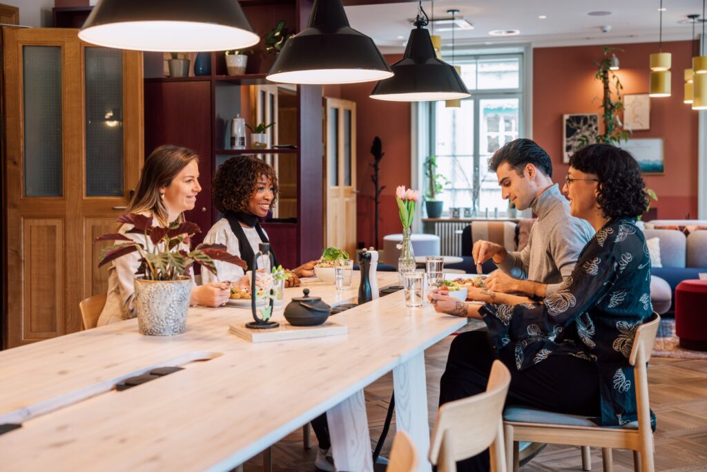 Vier Personen essen gemeinsam am Holztisch, genießen die Atmosphäre und tauschen sich in entspannter Runde aus.