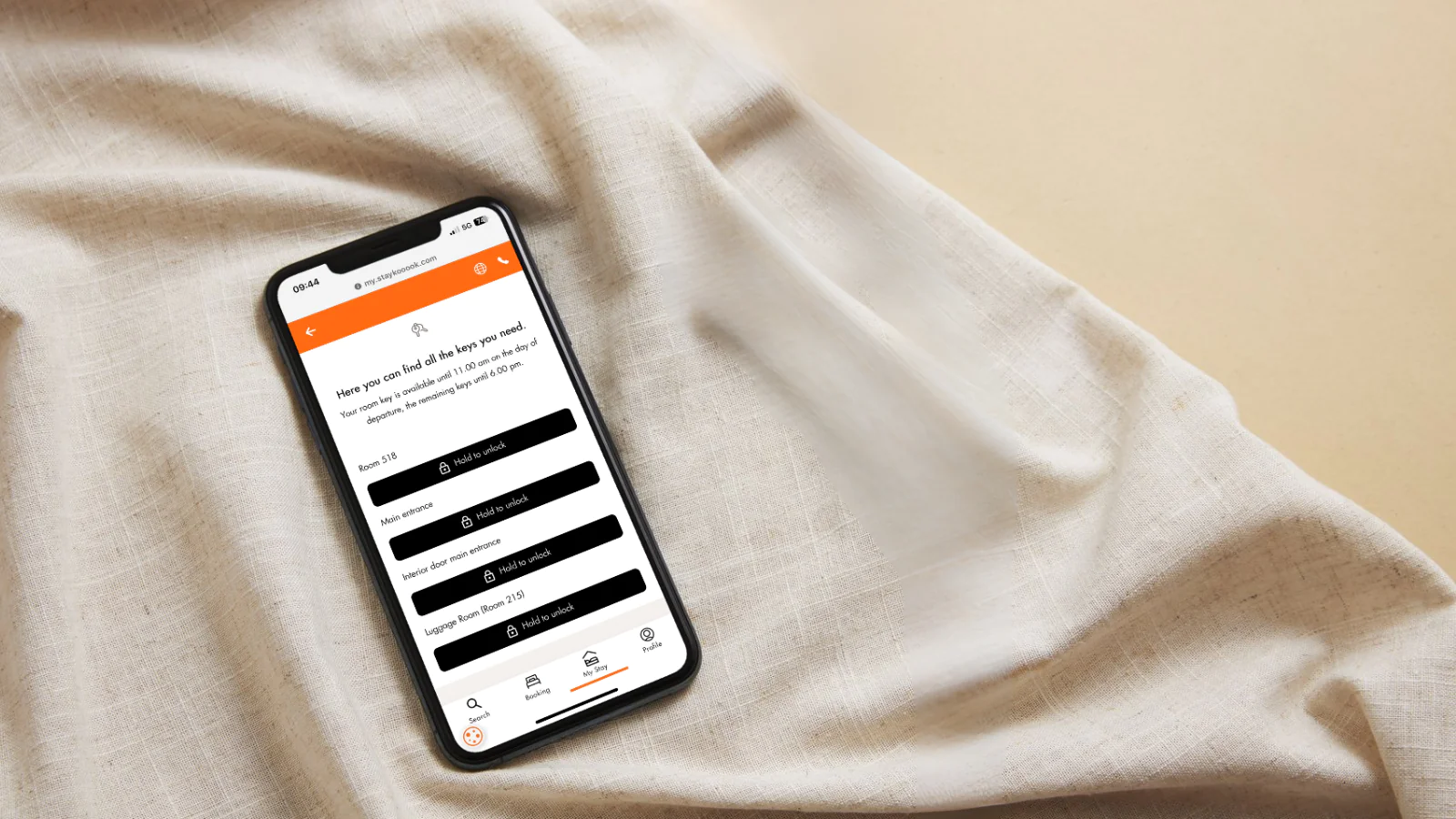 Smartphone mit digitalen Zimmerschlüsseln in der Stay KooooK Web App auf hellem Stoff.