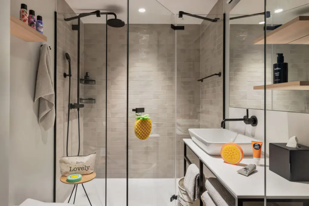 Bright bathroom with glass shower, rain and hand shower, vanity and decorative elements like bottle and brush.