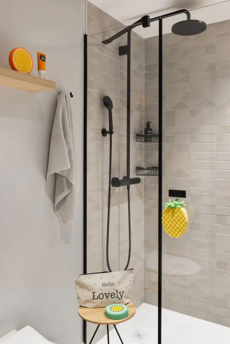 Bright bathroom with glass shower, rain and hand shower plus bath accessories like sponge and details.