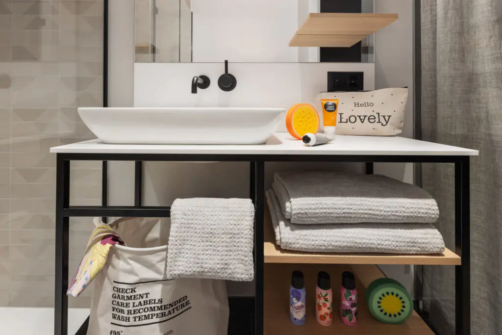 Vanity with black faucet, towels, laundry bag and cosmetics in a functional and modern design setting.